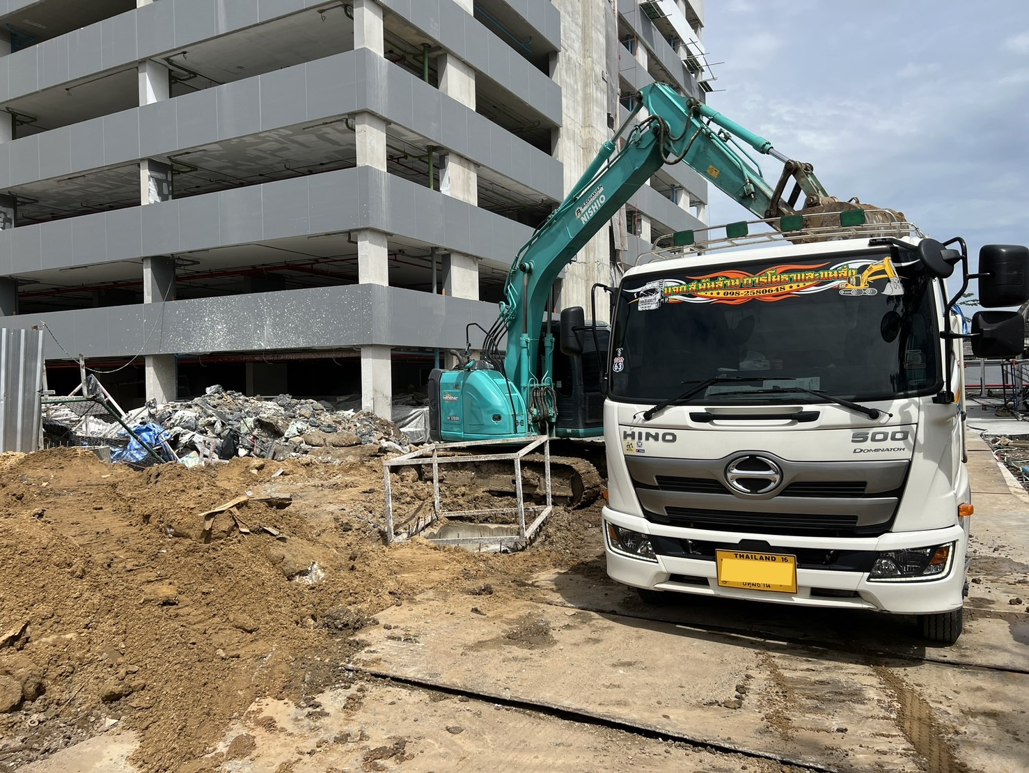 รถแบคโฮตักดินขึ้นรถบรรทุกหน้างานอาคาร - บริษัท ส.พันล้าน การโยธาและขนส่ง จำกัด